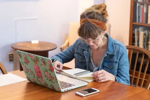 A student looks through their notes, a laptop is open in front of them